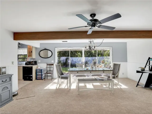 Dining room featuring light colored carpet, beamed ceiling, ceiling fan, and a chandelier