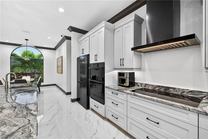Kitchen featuring light stone counters, wall chimney exhaust hood, light marble finish flooring, black appliances, and recessed lighting