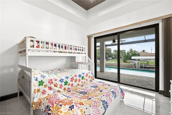 Bedroom featuring access to exterior, light marble finish floors, and a tray ceiling