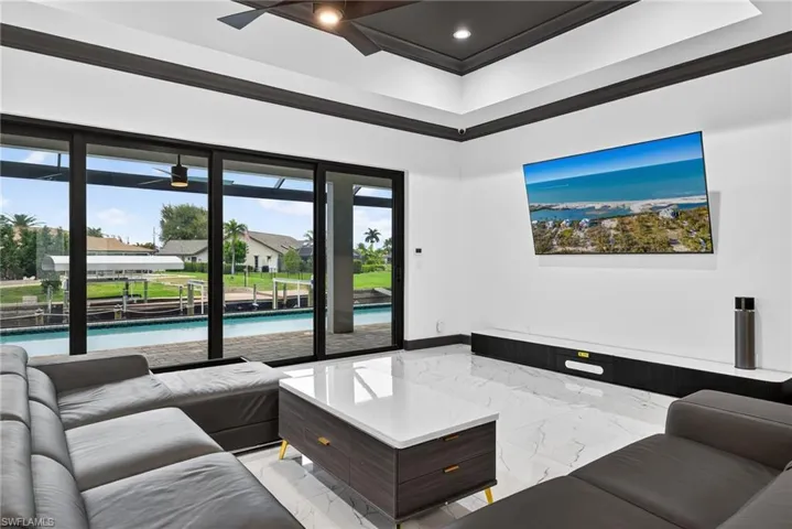 Living room featuring a raised ceiling, crown molding, recessed lighting, a ceiling fan, and light marble finish floors