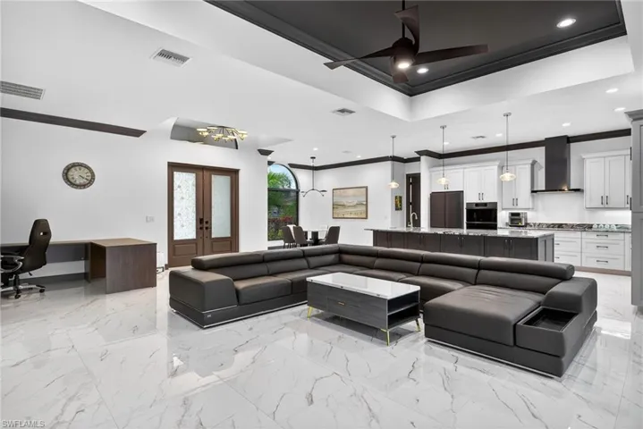Living room featuring crown molding, a raised ceiling, a desk, french doors, and a chandelier