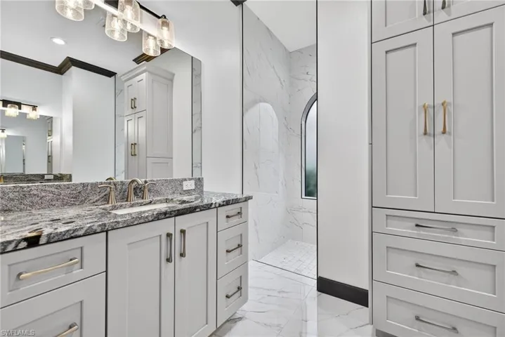 Bathroom featuring vanity, light marble finish floors, a marble finish shower, and crown molding