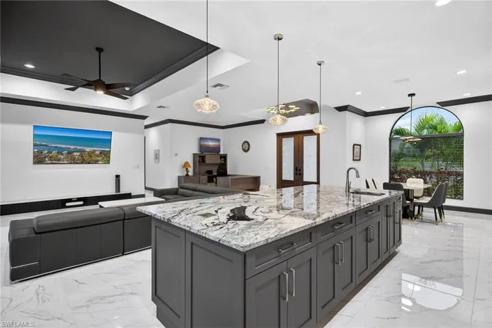 Kitchen featuring french doors, open floor plan, light stone counters, a spacious island, and ornamental molding