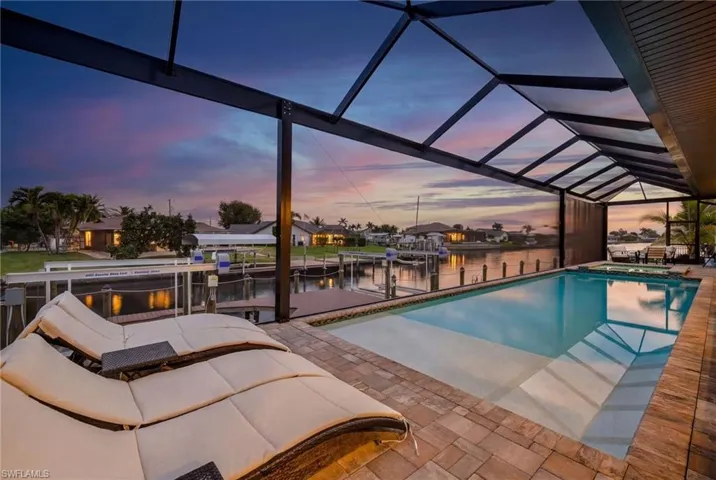Pool at dusk with boat lift, a water view, a sunroom, a boat dock, and a pool with connected hot tub