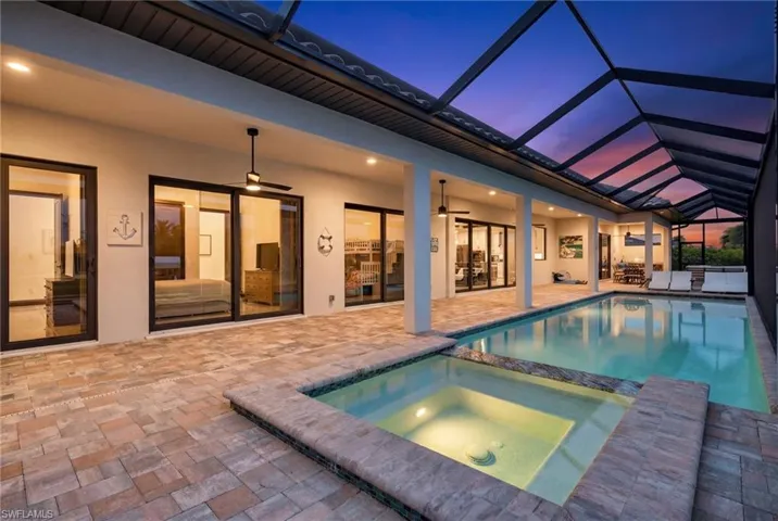 View of swimming pool featuring a sunroom, a pool with connected hot tub, a patio, and glass enclosure