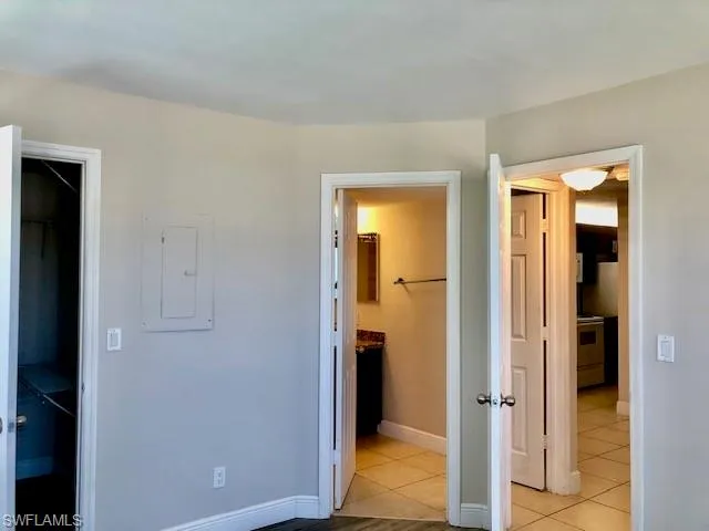 Unfurnished bedroom with electric panel, a spacious closet, ensuite bath, and light tile patterned flooring