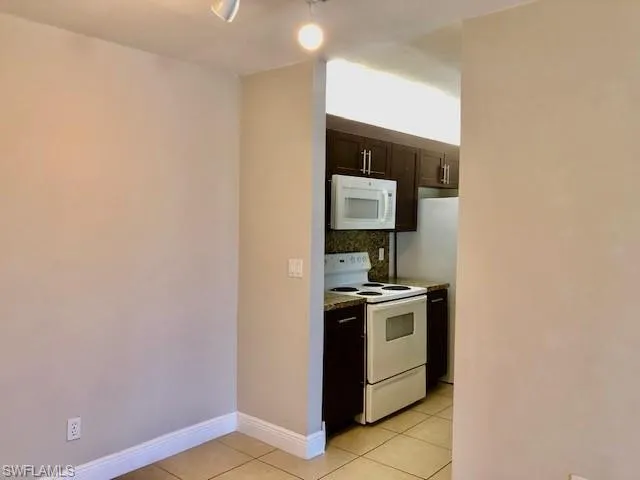 Kitchen featuring dark wood finish cabinets, white appliances, light tile patterned floors, decorative backsplash, and light countertops
