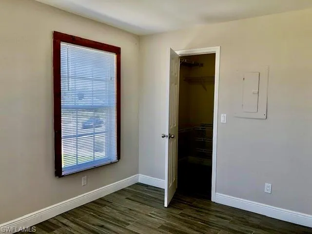 Unfurnished bedroom with a spacious closet, dark wood-style flooring, and electric panel