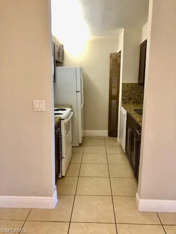 Kitchen with dark stone countertops, light tile patterned floors, white appliances, dark wood finish cabinetry, and decorative backsplash