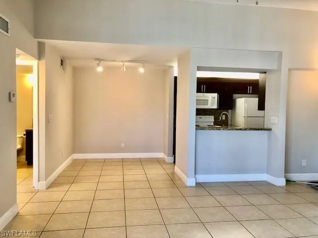 Kitchen featuring white appliances, dark wood finish cabinets, dark stone countertops, light tile patterned floors, and track lighting