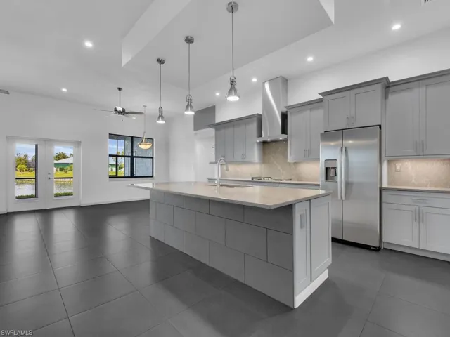 Kitchen with gray cabinetry, a sink, stainless steel fridge with ice dispenser, wall chimney range hood, and ceiling fan