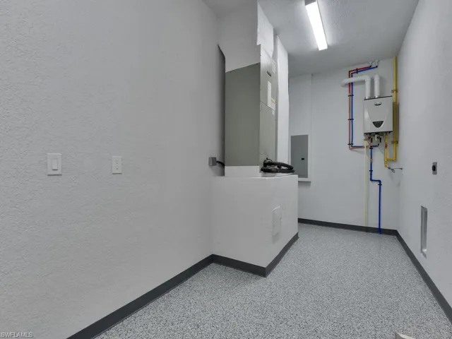 Hallway with electric panel, baseboards, speckled floor, and water heater