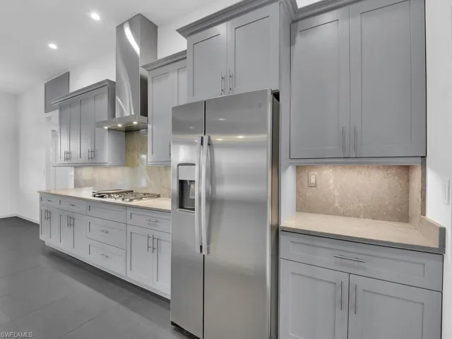 Kitchen with gray cabinetry, wall chimney range hood, light countertops, decorative backsplash, and stainless steel appliances