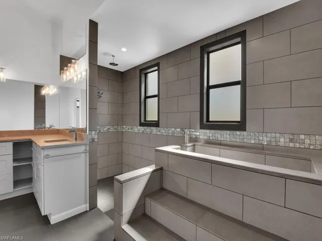 Bathroom featuring a walk in shower, tile walls, and vanity