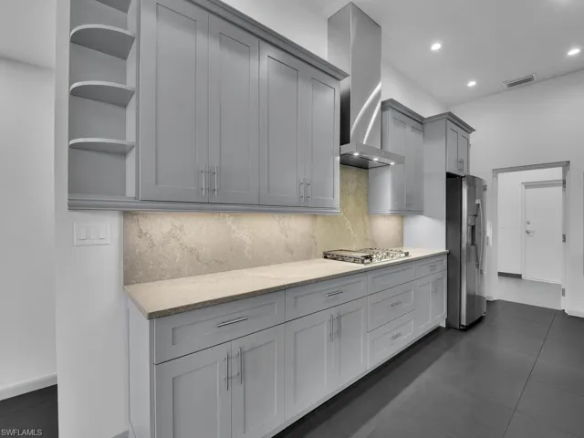 Kitchen with gray cabinetry, open shelves, tasteful backsplash, appliances with stainless steel finishes, and wall chimney range hood