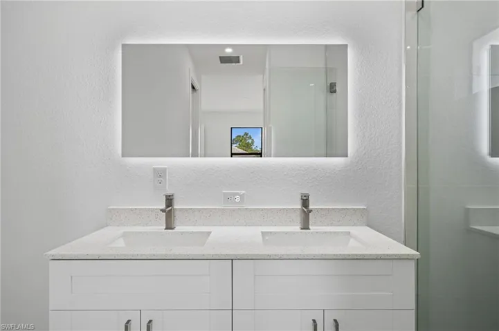 Bathroom with a textured wall, double vanity, and a shower stall