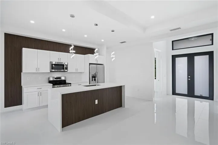 Kitchen featuring an island with sink, white cabinets, stainless steel appliances, and hanging light fixtures