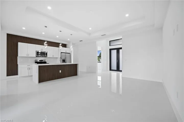 Kitchen with open floor plan, a center island with sink, white cabinets, stainless steel appliances, and hanging light fixtures