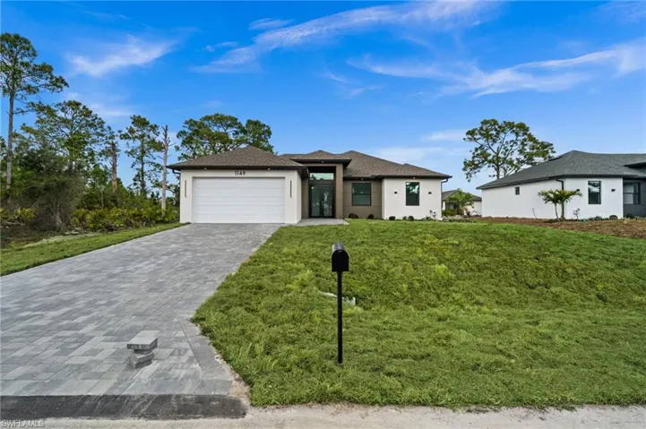 Prairie-style home featuring an attached garage, stucco siding, decorative driveway, a front lawn, and roof with shingles