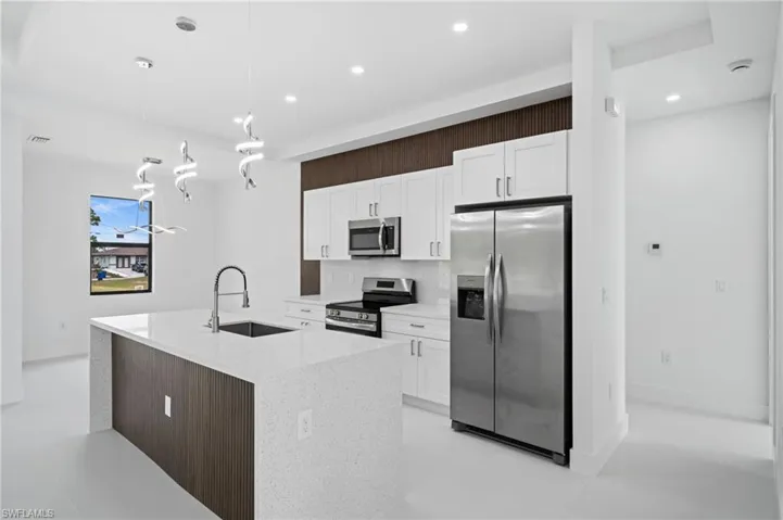 Kitchen with stainless steel appliances, an island with sink, light stone counters, white cabinets, and hanging light fixtures
