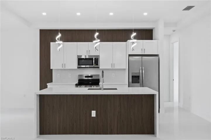 Kitchen featuring light stone counters, an island with sink, white cabinets, and stainless steel appliances