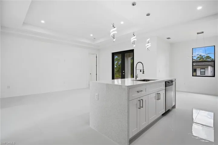 Kitchen with a center island with sink, light stone countertops, white cabinetry, pendant lighting, and a tray ceiling