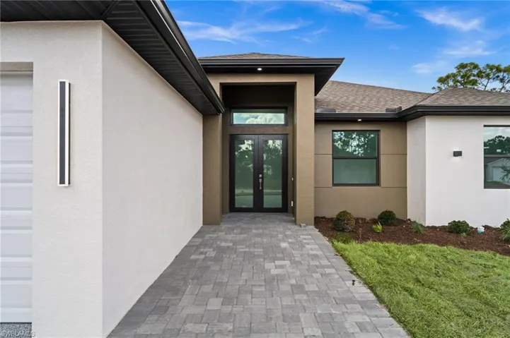 View of exterior entry featuring stucco siding, roof with shingles, and french doors