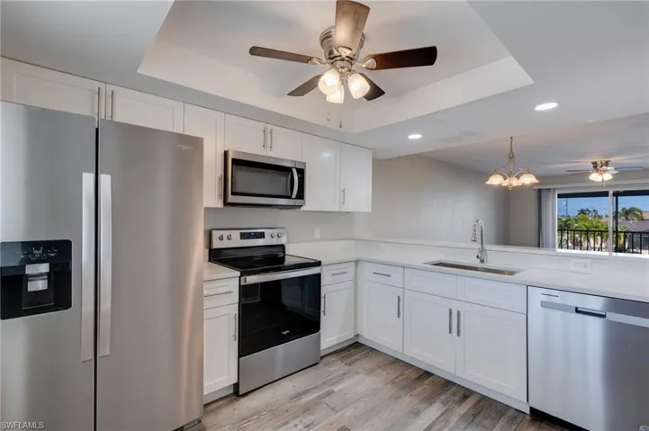 Kitchen featuring a ceiling fan, stainless steel appliances, a tray ceiling, white cabinetry, and recessed lighting