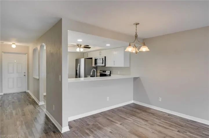 Kitchen with a peninsula, light wood-style flooring, white cabinetry, hanging light fixtures, and recessed lighting