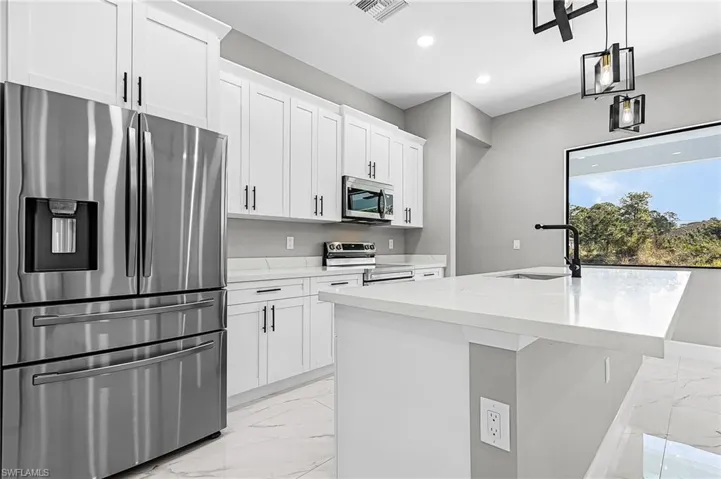 Kitchen featuring stainless steel appliances, a kitchen island with sink, light porcelain finish flooring, white cabinetry, and pendant lighting