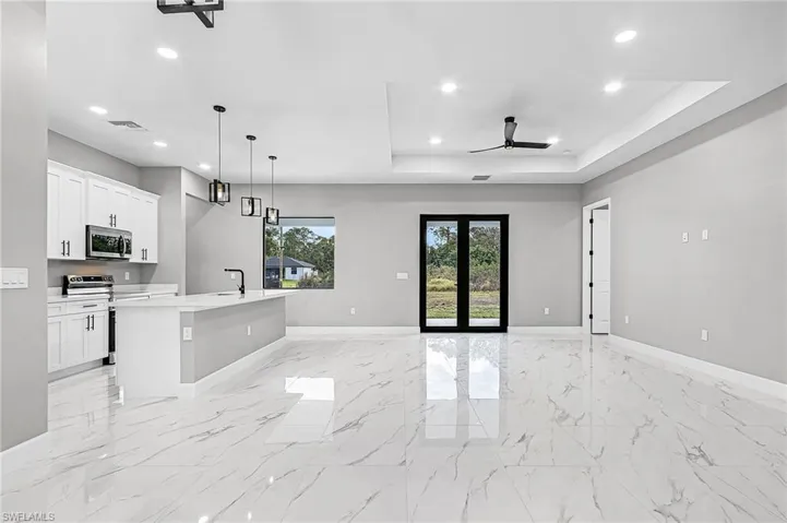 Kitchen with an island with sink, stainless steel appliances, white cabinetry, open floor plan, and pendant lighting