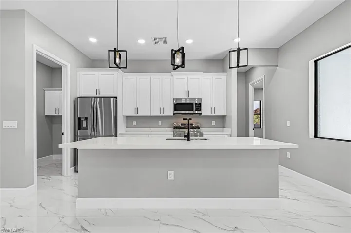 Kitchen featuring white cabinetry, light stone countertops, stainless steel appliances, an island with sink, and decorative light fixtures