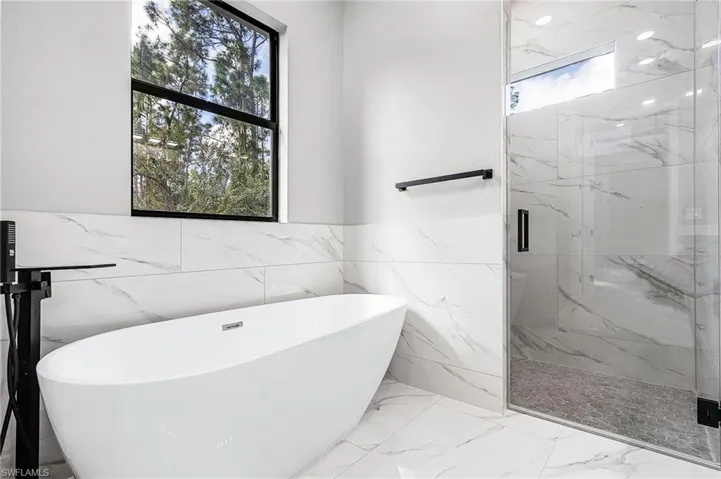 Full bathroom with a marble finish shower, light porcelain finish floors, a freestanding tub, wainscoting, and tile walls