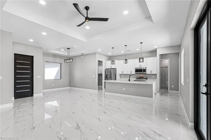 Kitchen with a tray ceiling, a ceiling fan, white cabinets, an island with sink, and stainless steel appliances