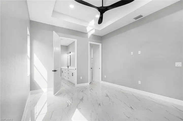 Unfurnished bedroom with ensuite bathroom, a tray ceiling, recessed lighting, a ceiling fan, and light porcelain finish floors