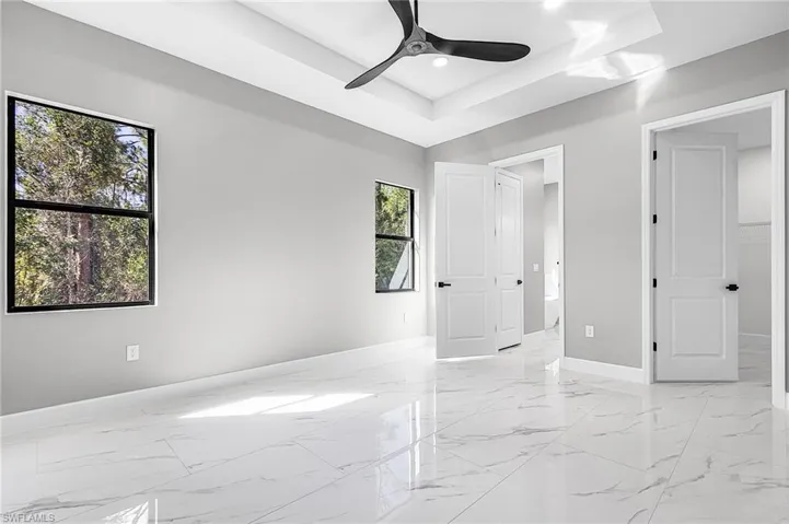 Primary bedroom with en suite with a tray ceiling, ceiling fan, and light marble finish flooring