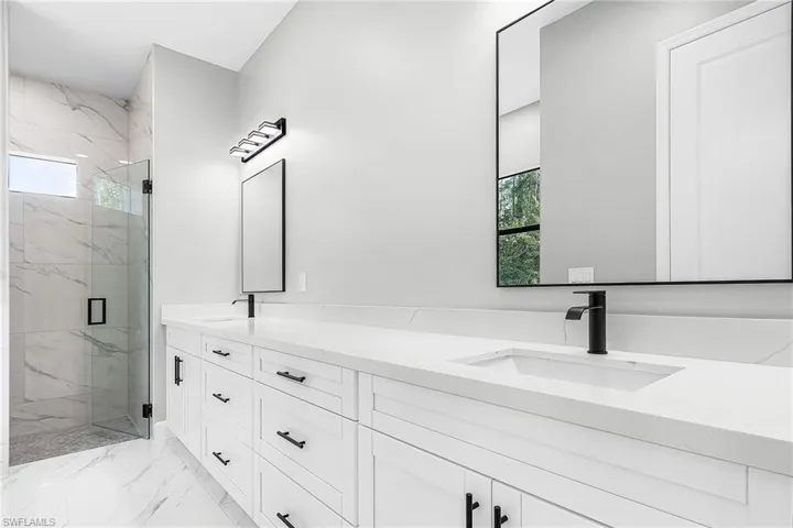 Bathroom with a porcelain finish shower, double vanity, and light marble finish floors