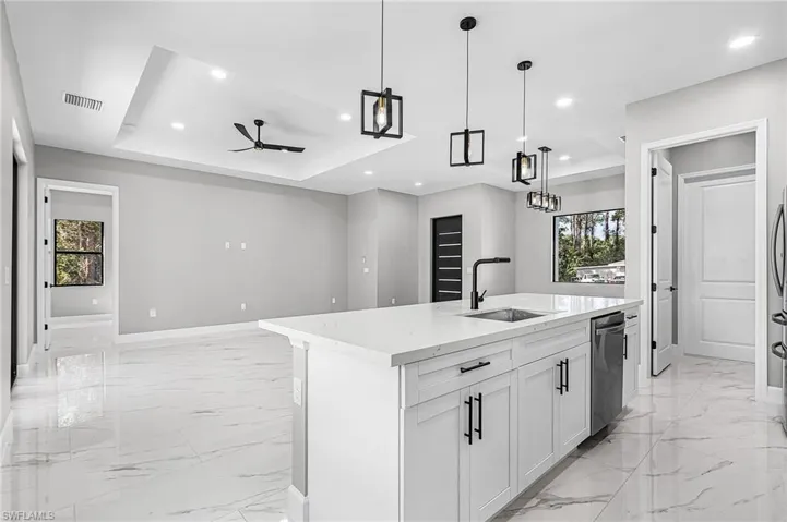 Kitchen with open floor plan, a kitchen island with sink, hanging light fixtures, white cabinets, and light stone countertops