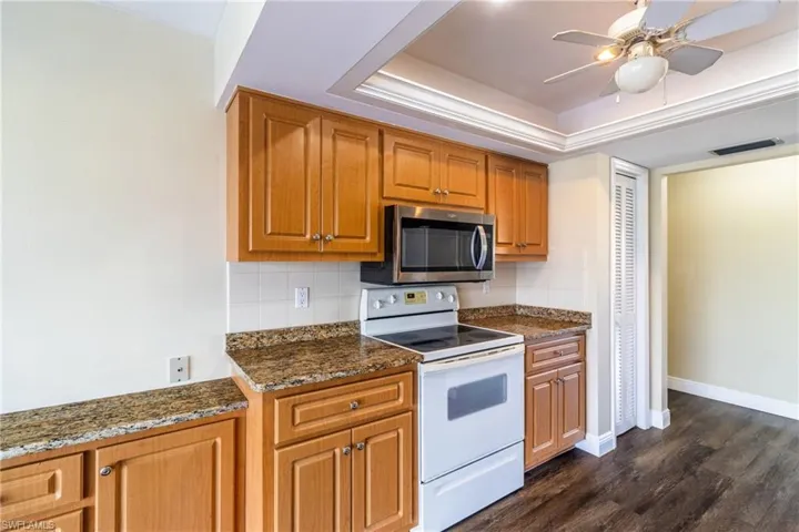 Kitchen featuring white range with electric stovetop, dark stone counters, ceiling fan, a raised ceiling, and wood finish cabinetry