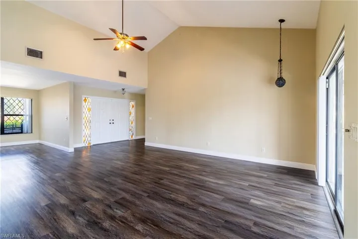 Unfurnished living room with a ceiling fan, vaulted ceiling, and dark wood-style flooring