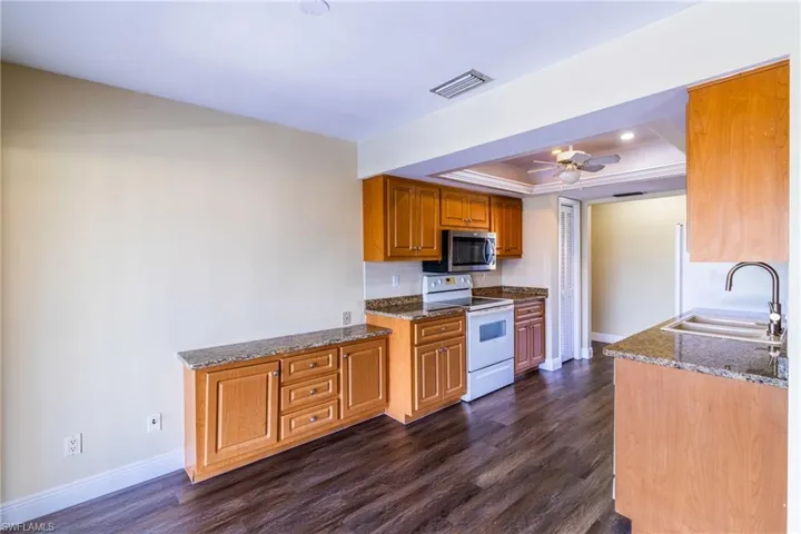 Kitchen with dark stone counters, electric stove, a raised ceiling, ceiling fan, and dark wood-style floors