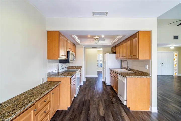 Kitchen featuring dark stone counters, white appliances, a ceiling fan, dark wood-style floors, and a raised ceiling