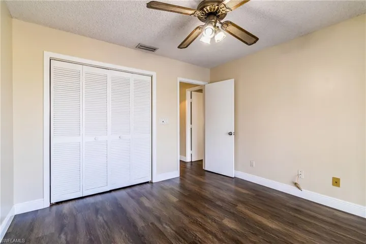 Unfurnished bedroom with a textured ceiling, dark wood-type flooring, ceiling fan, and a closet