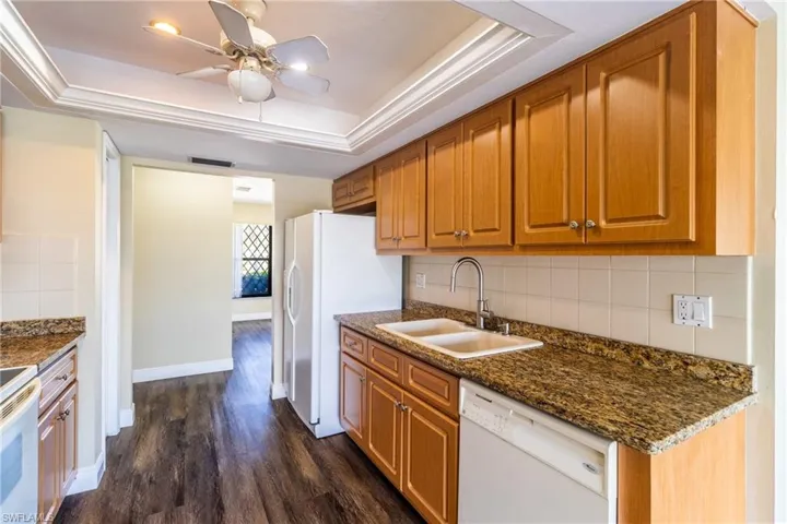 Kitchen featuring a tray ceiling, white appliances, decorative backsplash, wood finish cabinets, and ceiling fan