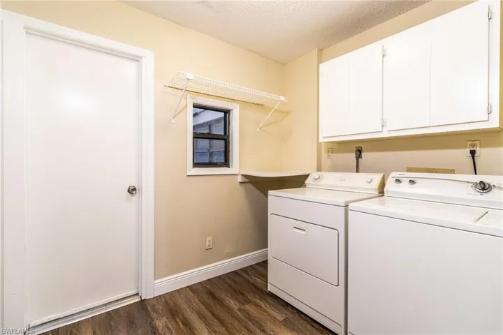Laundry area with a textured ceiling, dark wood-style floors, washer and clothes dryer, and cabinet space