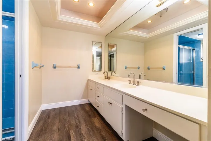 Bathroom with a tray ceiling, a stall shower, double vanity, dark wood-type flooring, and recessed lighting