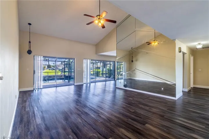 Unfurnished living room featuring ceiling fan, lofted ceiling, and dark wood-style flooring