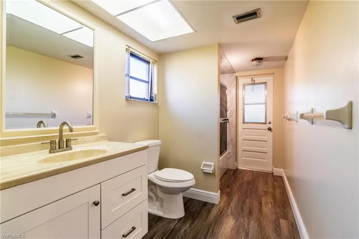 Bathroom with enclosed tub / shower combo, vanity, and dark wood-type flooring