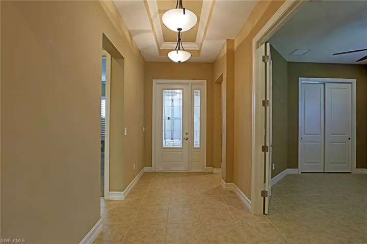 Foyer entrance with a tray ceiling, light tile patterned floors, and a ceiling fan