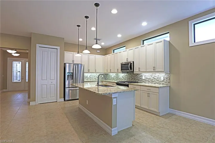 Kitchen featuring stainless steel appliances, light stone countertops, backsplash, an island with sink, and hanging light fixtures